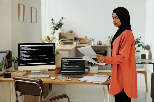 Jovem programadora ou contadora muçulmana olhando papéis