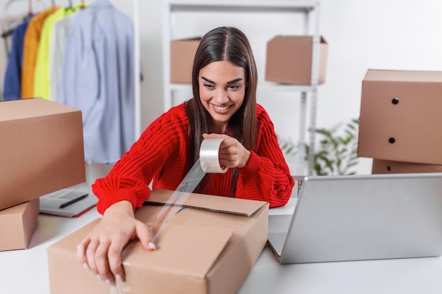 Jovem, proprietária de produtos de embalagem de pequenas empresas em caixas, preparando-o para entrega. Mulheres embalando o pacote com seus produtos que ela vende on-line