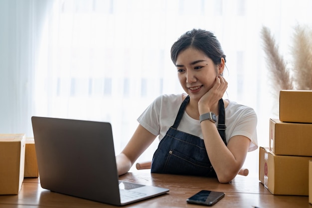 Jovem proprietário de uma pequena empresa de compras on-line em casa confirma pedidos de clientes com telefones celulares preparando o produto do pacote no fundo empresário de pme ou conceito de estilo de vida freelance