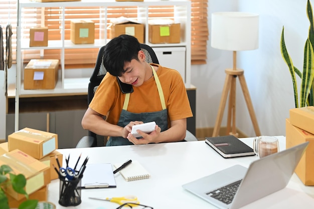 Jovem proprietário de uma pequena empresa falando no celular para receber o pedido do cliente