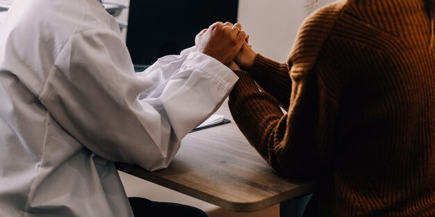 Foto jovem psicóloga segurando a mão de seu paciente necessitado enquanto a consultava após discussão do problema