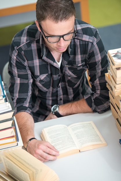 Jovem que estuda na biblioteca da faculdade com uma pilha de livros