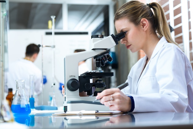 Jovem que olha através do microscópio em laboratório.