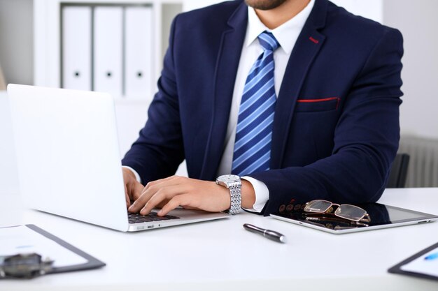 Jovem que trabalha com as mãos do homem do computador portátil na pessoa de negócios do notebook no local de trabalho