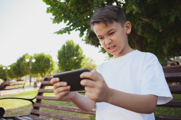 Jovem rapaz asiático jogando jogos em seu telefone inteligente no parque