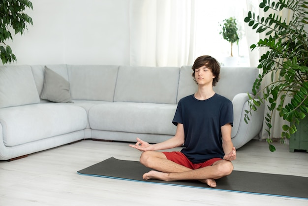 Jovem rapaz com cabelos longos faz yoga em casa