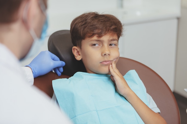 Foto jovem rapaz com dor de dente, sentado em uma cadeira odontológica durante o exame dentário