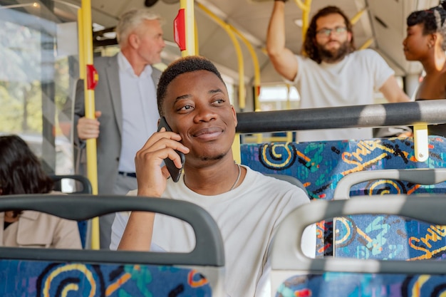 Jovem rapaz de pele escura falando ao telefone enquanto está sentado em uma cadeira olhando pela janela sorrindo