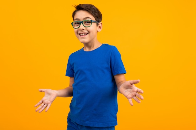 Jovem rapaz em uma camiseta azul com óculos estende as mãos em direções diferentes em amarelo com espaço de cópia
