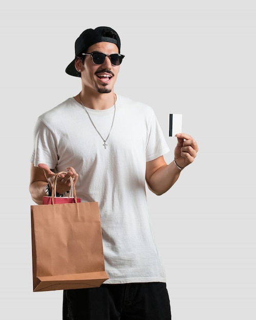 Foto jovem, rapper, homem, alegre, e, sorrindo, muito, excitado, segurando, a, novo, cartão banco, e, bolsas para compras, pronto, ir, shopping