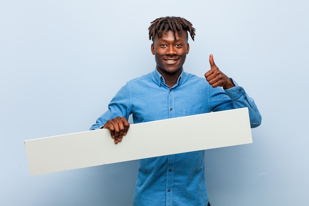 Jovem rasta negro segurando um cartaz sorrindo e levantando o polegar