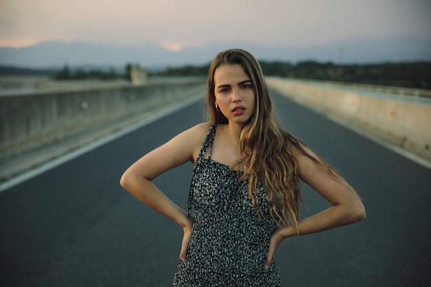 Jovem rebelde bonita na estrada vazia ao pôr do sol