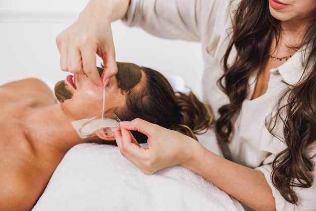 Jovem recebendo tapa-olhos e tratamento facial com lama de algas no spa.