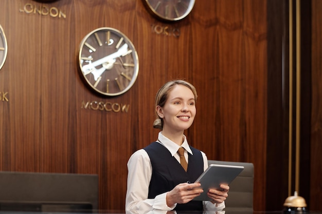 Jovem recepcionista feminina sorridente do luxuoso hotel segurando o tablet