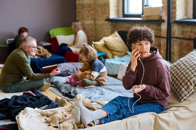 Jovem refugiada ligando pelo smartphone enquanto está sentado no lugar de dormir