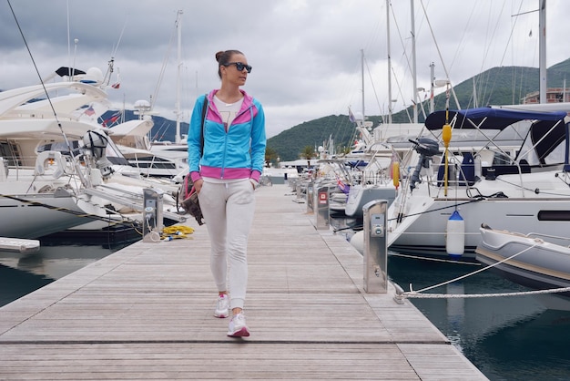 jovem relaxada andando na marina com barcos de iate em bacground