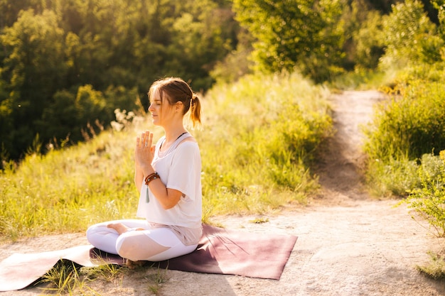Jovem relaxada está meditando em posição de lótus com os olhos fechados, sentado no tapete de ioga Instrutor de ioga feminino fazendo pose de namaste Senhora desfrutando de meditação Senhora oração meditando em Namaste mudra