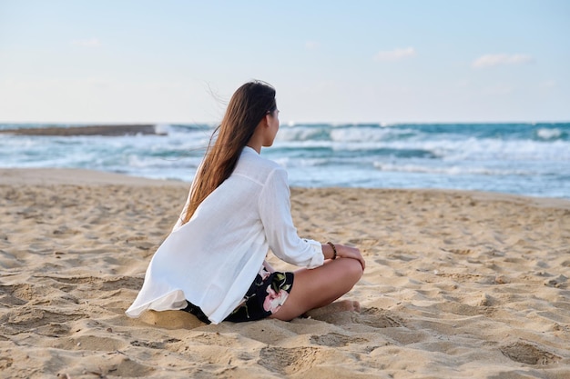 Jovem relaxada sentada em posição de lótus na natureza do mar de manhã de praia