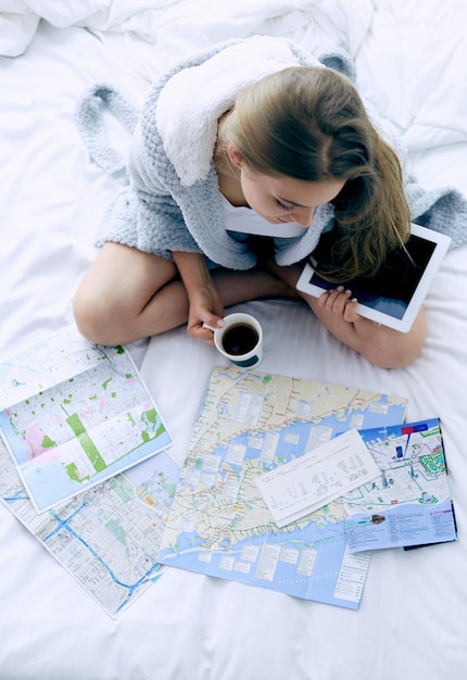 Foto jovem relaxada sentada na cama com uma xícara de café e um tablet digital