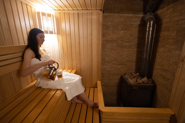 Jovem relaxando e suando na sauna quente enrolada em toalha Garota na sauna Interior da sauna finlandesa