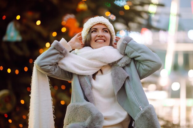 Jovem relaxante bebendo café na feira festiva de Natal. Férias de inverno. Luzes ao redor.