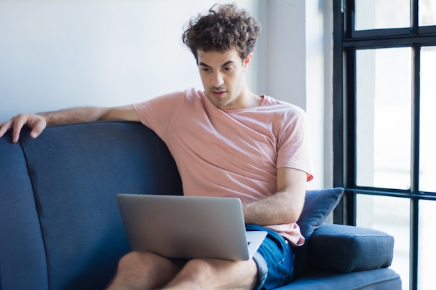 Jovem relaxante no sofá com um laptop