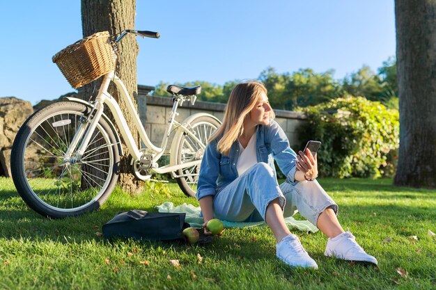 Jovem relaxante sentada na grama no parque usando smartphone