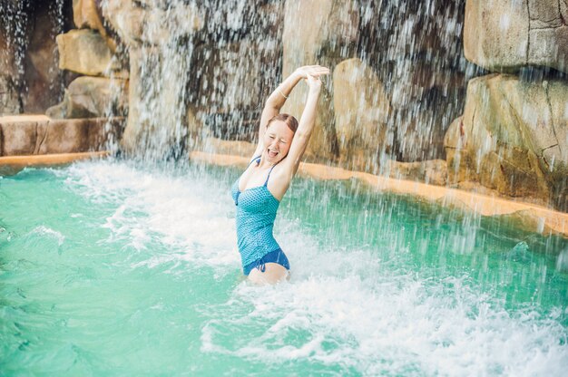 Jovem relaxante sob uma cachoeira no parque aquático