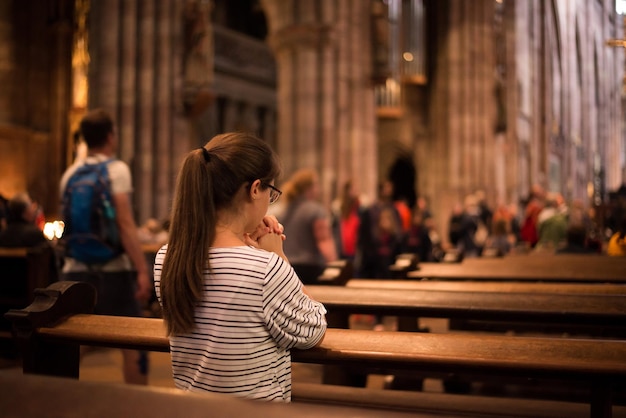 Jovem religiosa de óculos com longos cabelos escuros orando na catedral católica