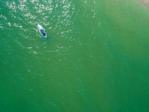 Jovem remando na prancha de SUP na praia tropical Férias de verão ativas com prancha de remo