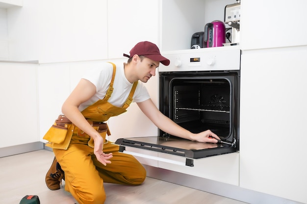 jovem reparador no forno de fixação do vestuário de proteção na cozinha.