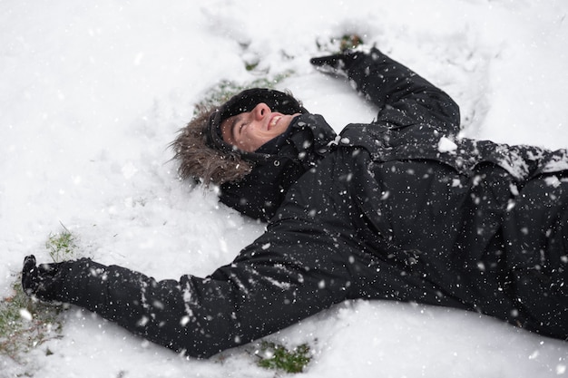 Jovem rindo, com expressão feliz, coberto de neve, deitado no chão na neve.