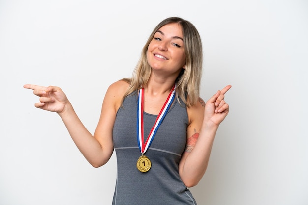 Foto jovem romena com medalhas isoladas no fundo branco, apontando o dedo para as laterais e feliz