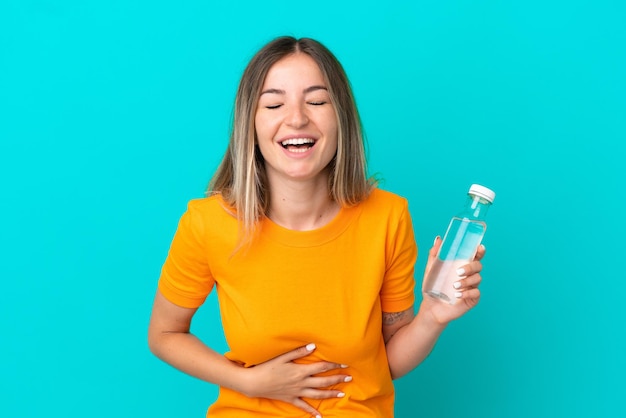 Jovem romena com uma garrafa de água isolada em um fundo azul sorrindo muito