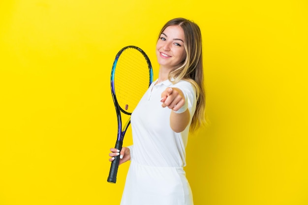 Jovem romena isolada em fundo amarelo jogando tênis e apontando para a frente