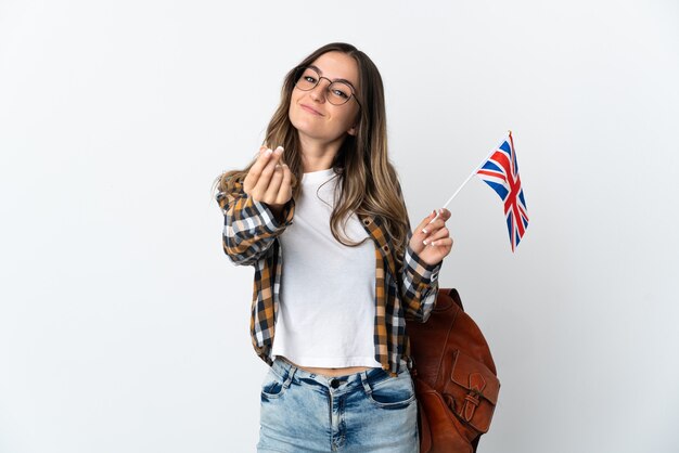 Jovem romena segurando uma bandeira do Reino Unido isolada na parede branca fazendo gesto de dinheiro