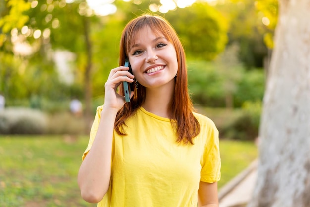 Jovem ruiva bonita ao ar livre mantendo uma conversa com o celular com alguém