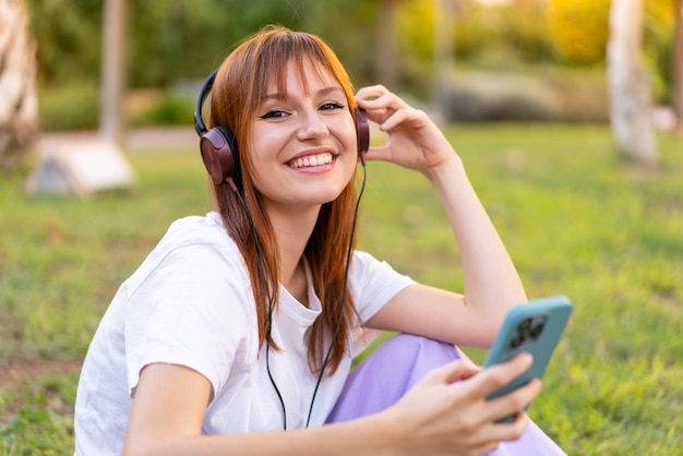 Jovem ruiva bonita ao ar livre ouvindo música com o celular