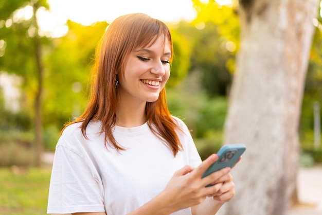 Jovem ruiva bonita ao ar livre usando telefone celular com expressão feliz