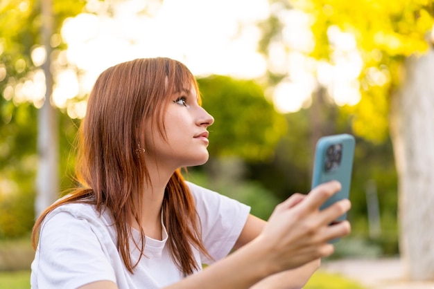 Jovem ruiva bonita ao ar livre usando telefone celular