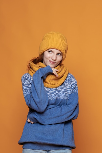 Jovem ruiva com um chapéu quente e uma camisola de malha em um fundo amarelo