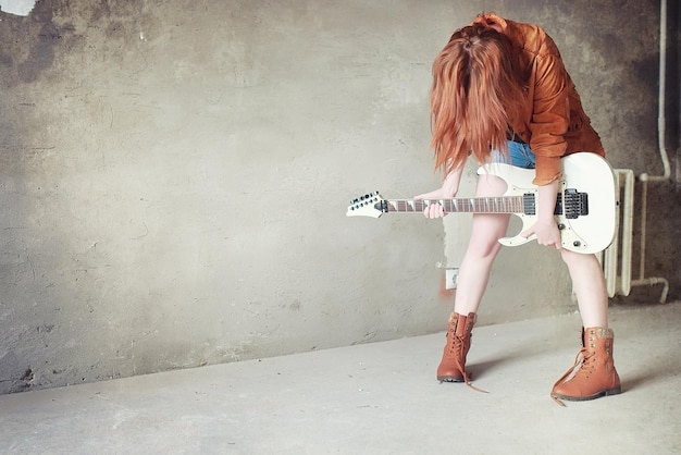 Jovem ruiva com uma guitarra elétrica garota de músico de rock em uma jaqueta de couro ela é uma linda cantora e artista de rock