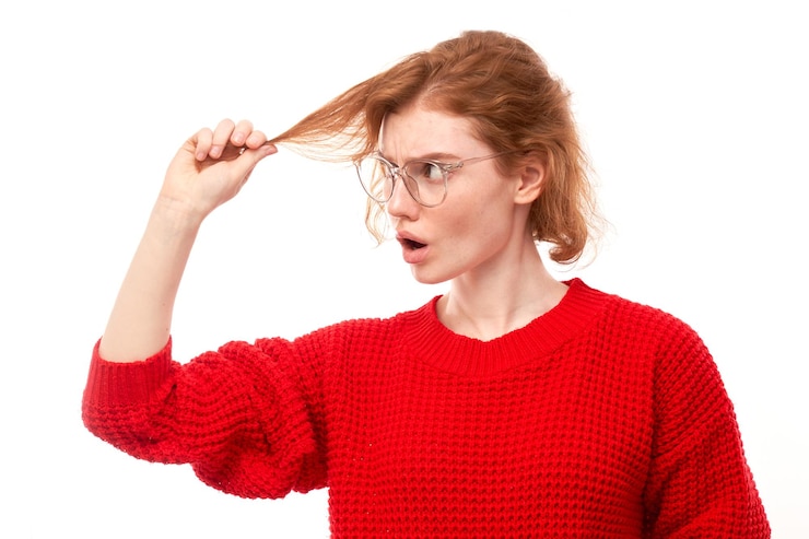 Foto jovem ruiva de retrato tocando o cabelo com rosto descontente isolado no fundo branco do estúdio conceito de cabelo danificado