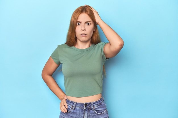 Jovem ruiva em fundo azul ficando chocada por ter se lembrado de uma reunião importante