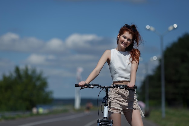 Jovem ruiva em shorts e tops posando em pé com bicicleta