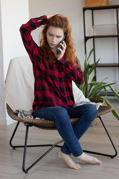 Jovem ruiva falando ao celular em casa na cozinha