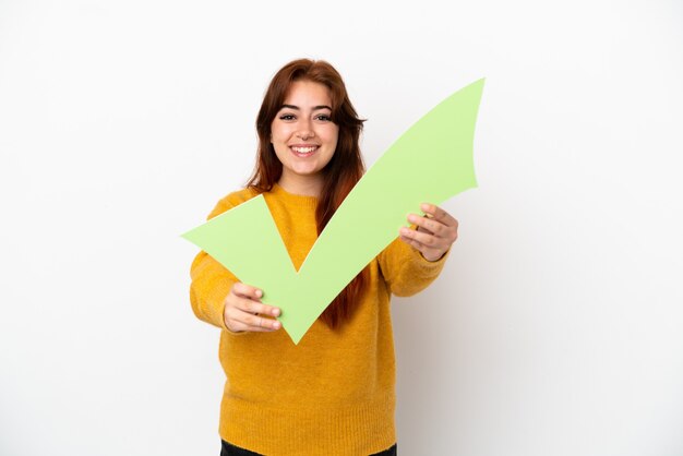 Jovem ruiva isolada em um fundo branco segurando um ícone de cheque com uma expressão feliz