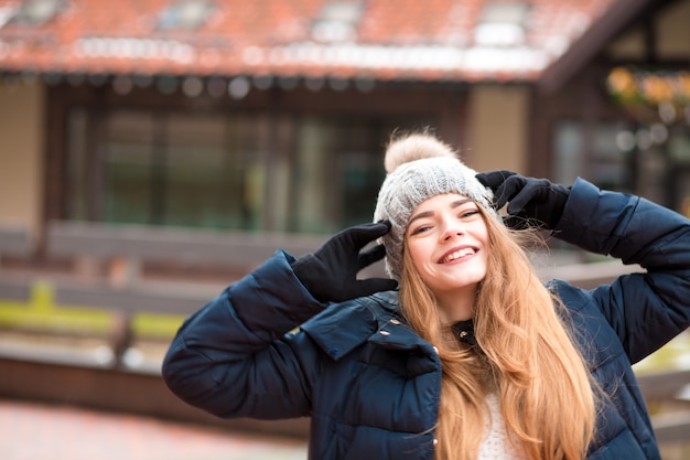 Jovem ruiva positiva, vestindo um casaco de inverno preto e chapéu de malha, posando na rua em kiev