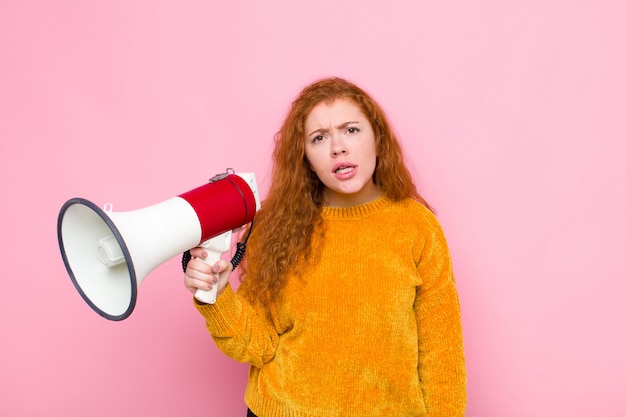 Jovem ruiva se sentindo confusa e confusa, com uma expressão estúpida e aturdida, olhando para algo inesperado com um megafone