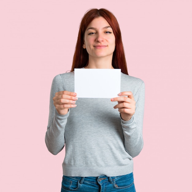 Foto jovem ruiva segurando um cartaz branco vazio para inserir um conceito em fundo rosa isolado